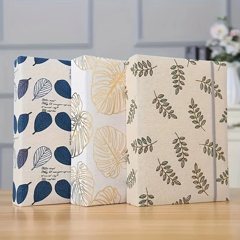 Ein Set aus drei cremefarbenen Fotoalben mit botanischen Blattmustern und dunkelblauen Akzenten.