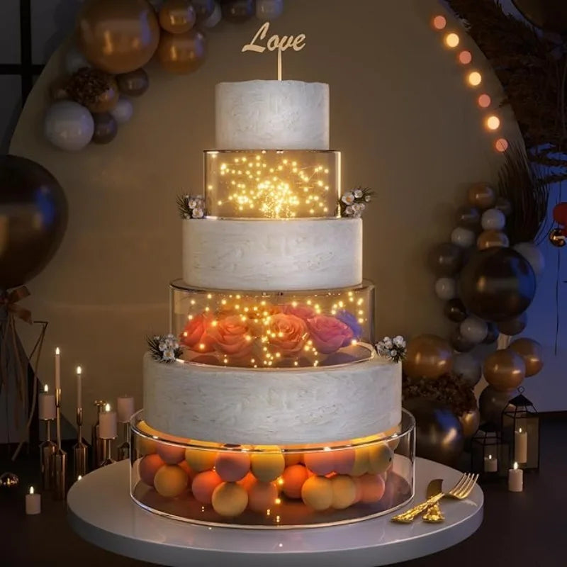 A four-tiered white cake display featuring orange and pink roses illuminated by warm LED lights.