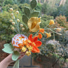 Un ramo de flores de ganchillo hechas a mano en tonos naranja, amarillo y verde contra un fondo exterior desenfocado.