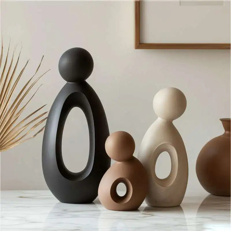 A set of modern resin family statues in matte black, beige, and terracotta on a white marble surface.
