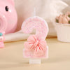 A pink number two candle decorated with glitter and a pink bow, set against a soft background.