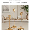 A set of three elegant gold-toned metal candlesticks displayed on a light surface.