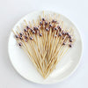 A plate holds numerous bamboo cocktail picks tipped with white pearl-colored beads.