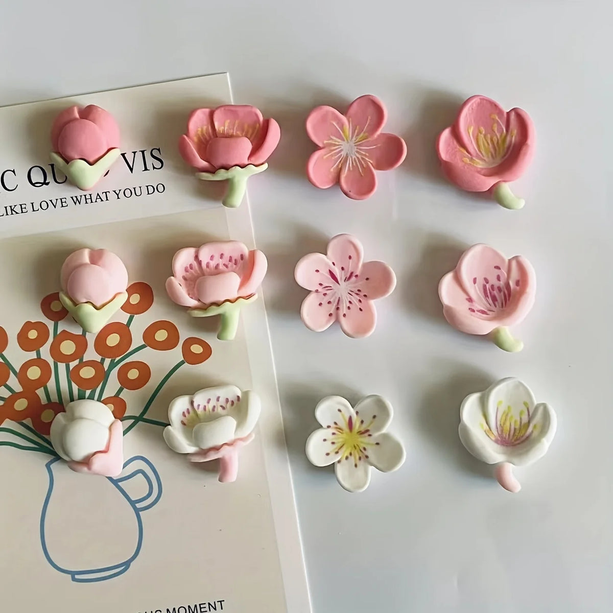A collection of 12 pink and white flower decorative fridge magnets arranged on a white surface.