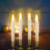 Four white pillar candles glowing in glass jars with warm light and golden illumination