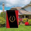 A black heritage garden flag with a gold laurel wreath design displayed in a yard.