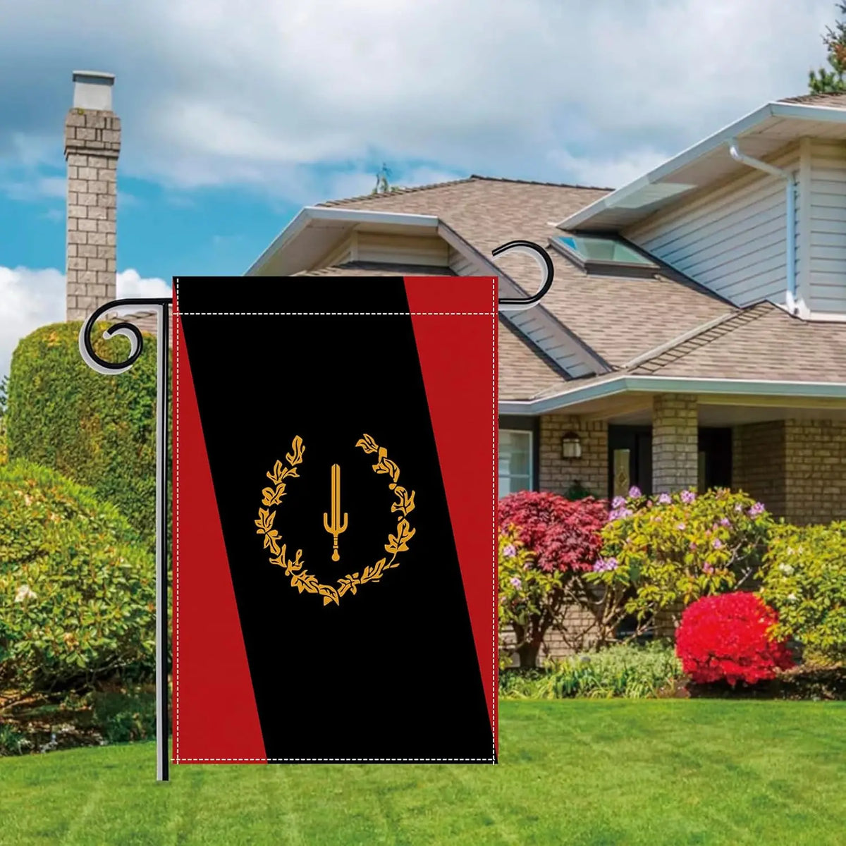 A black heritage garden flag with a gold laurel wreath design displayed in a yard.