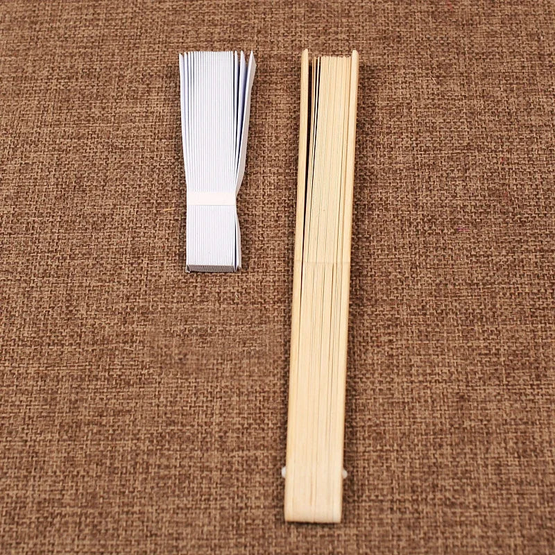 Un éventail squelette en bambou pliable en bois clair posé sur un tissu marron.