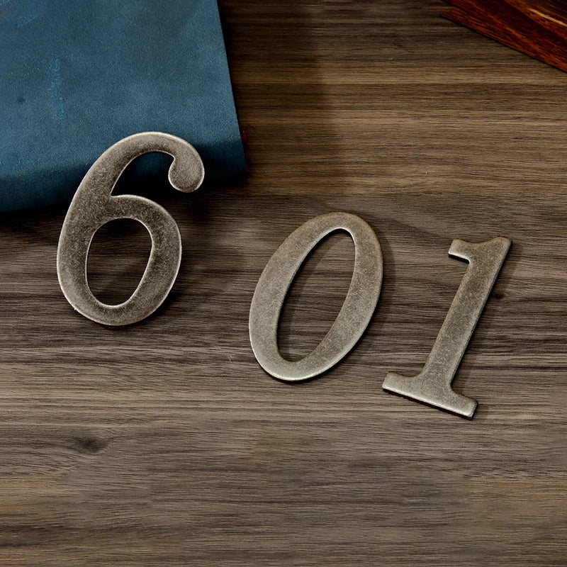 Magnetic silver house number featuring the digits 601 embossed on a dark wooden surface.