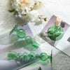 A set of three green wavy glass taper candle holders displayed on white paper with a lit candle.