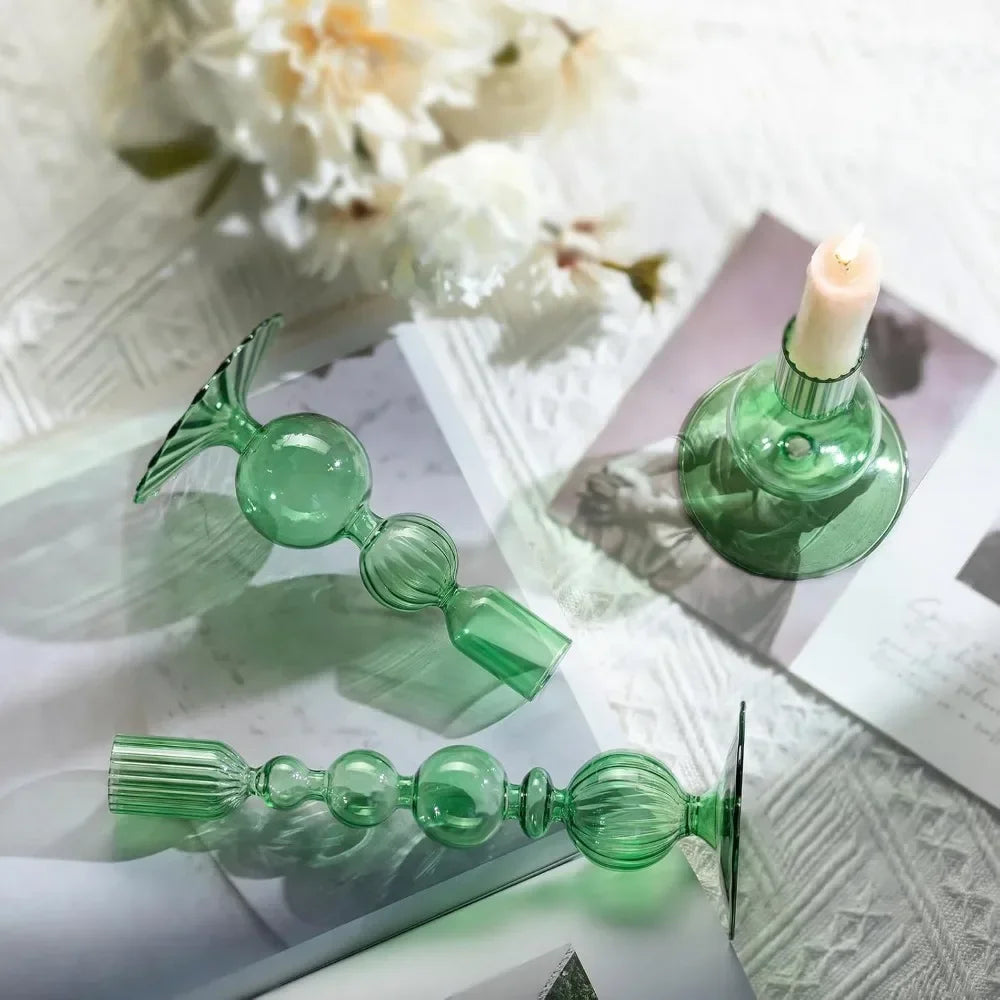 A set of three green wavy glass taper candle holders displayed on white paper with a lit candle.