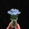 A hand holds a small glass vase filled with light blue handmade glass flowers against a black background.