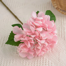 A cluster of pink artificial hydrangea florets on a white textured surface.