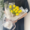 A bouquet of yellow artificial tulips wrapped in clear cellophane and tied with a sheer ribbon.