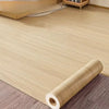 Roll of self-adhesive PVC wallpaper film with a wood grain texture lying on a wooden floor.