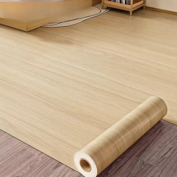 Roll of self-adhesive PVC wallpaper film with a wood grain texture lying on a wooden floor.