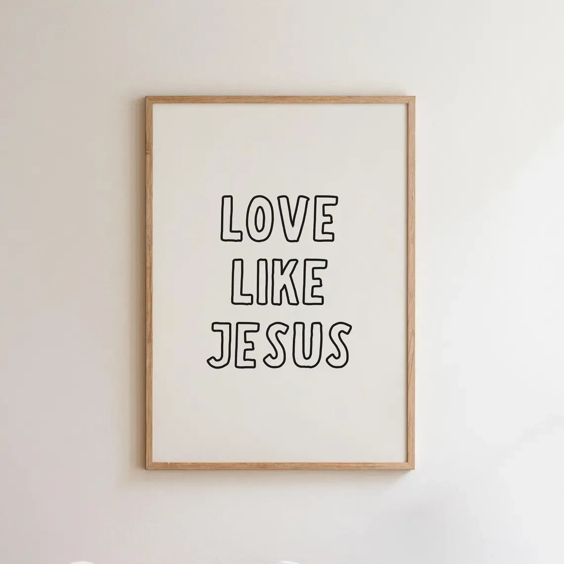 Framed wall art print with the text LOVE LIKE JESUS in black lettering on a white background and light wood frame