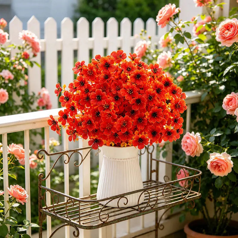 A vibrant bouquet of artificial orange-red pansy flowers in a white pot displayed on an outdoor railing.