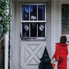 A person in a red costume stands in front of a window decorated with a scary Halloween banner.