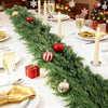 A realistic cedar garland decorated with red and gold ornaments, candles, and wrapped gifts on a white table.