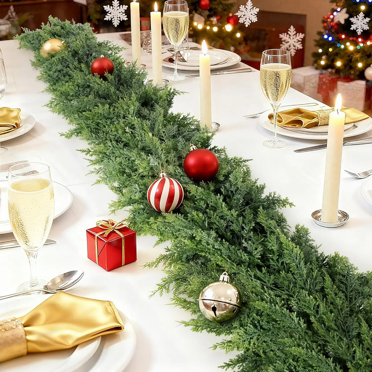 A realistic cedar garland decorated with red and gold ornaments, candles, and wrapped gifts on a white table.