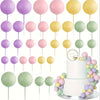 A set of twenty pastel colored ball cake toppers on sticks arranged around a two-tiered white cake.