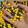 A hand holds a large quantity of pastel foam beads in yellow and dark gray colors for crafting.
