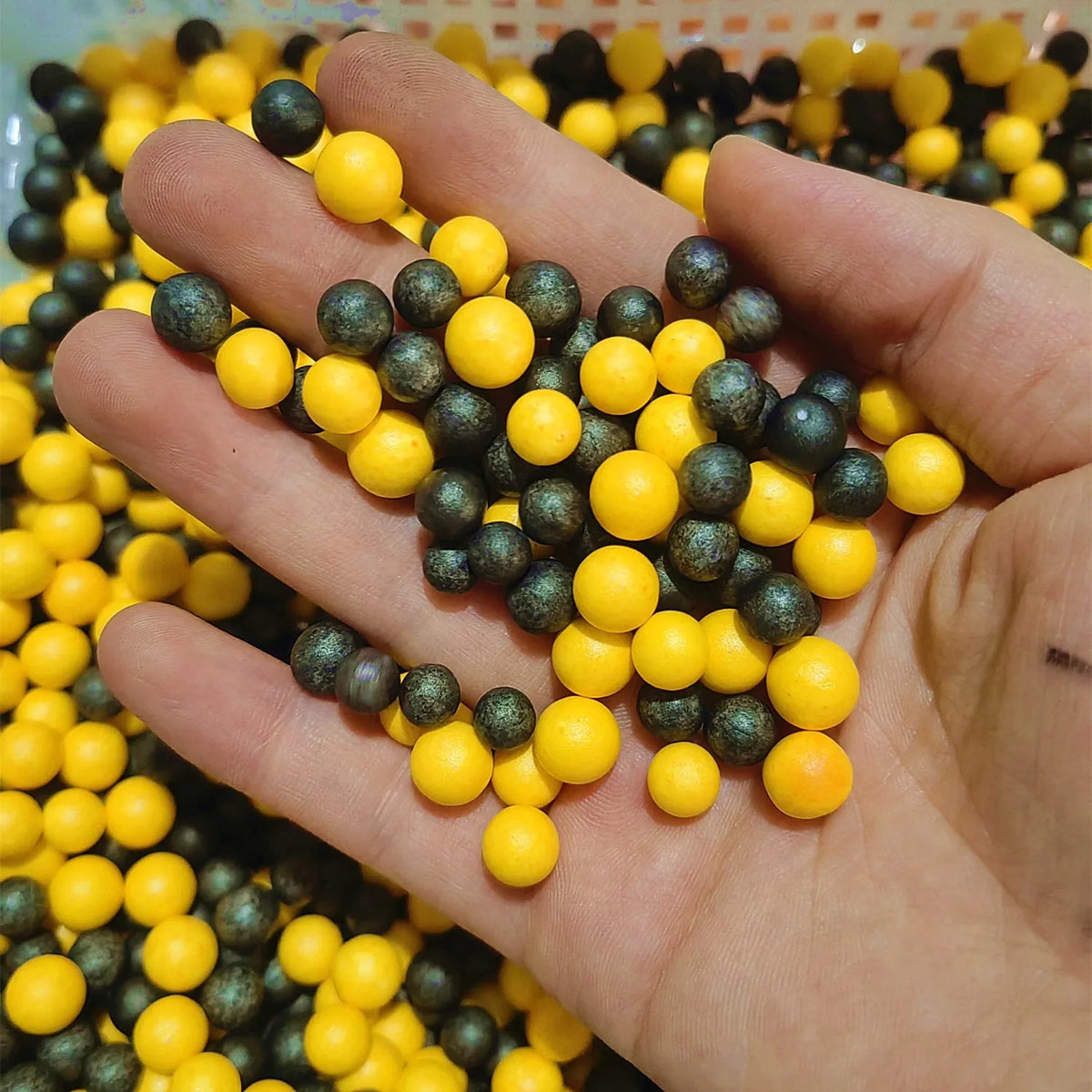 A hand holds a large quantity of pastel foam beads in yellow and dark gray colors for crafting.