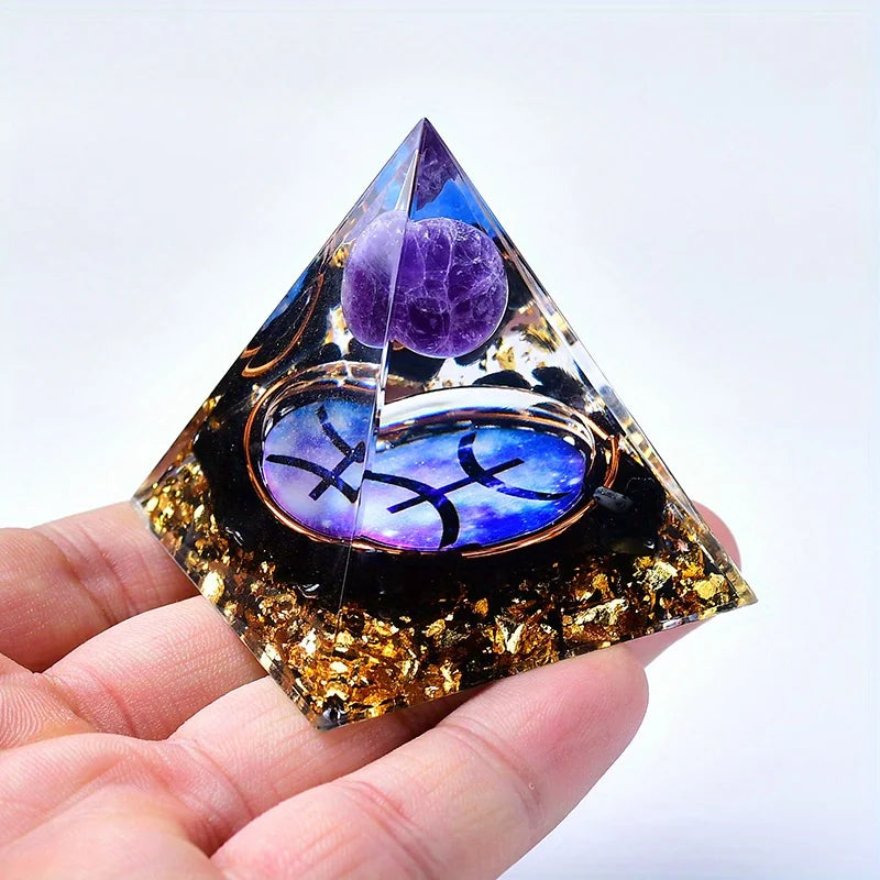 A clear pyramid-shaped crystal featuring purple amethyst and blue zodiac symbols, held in a hand.