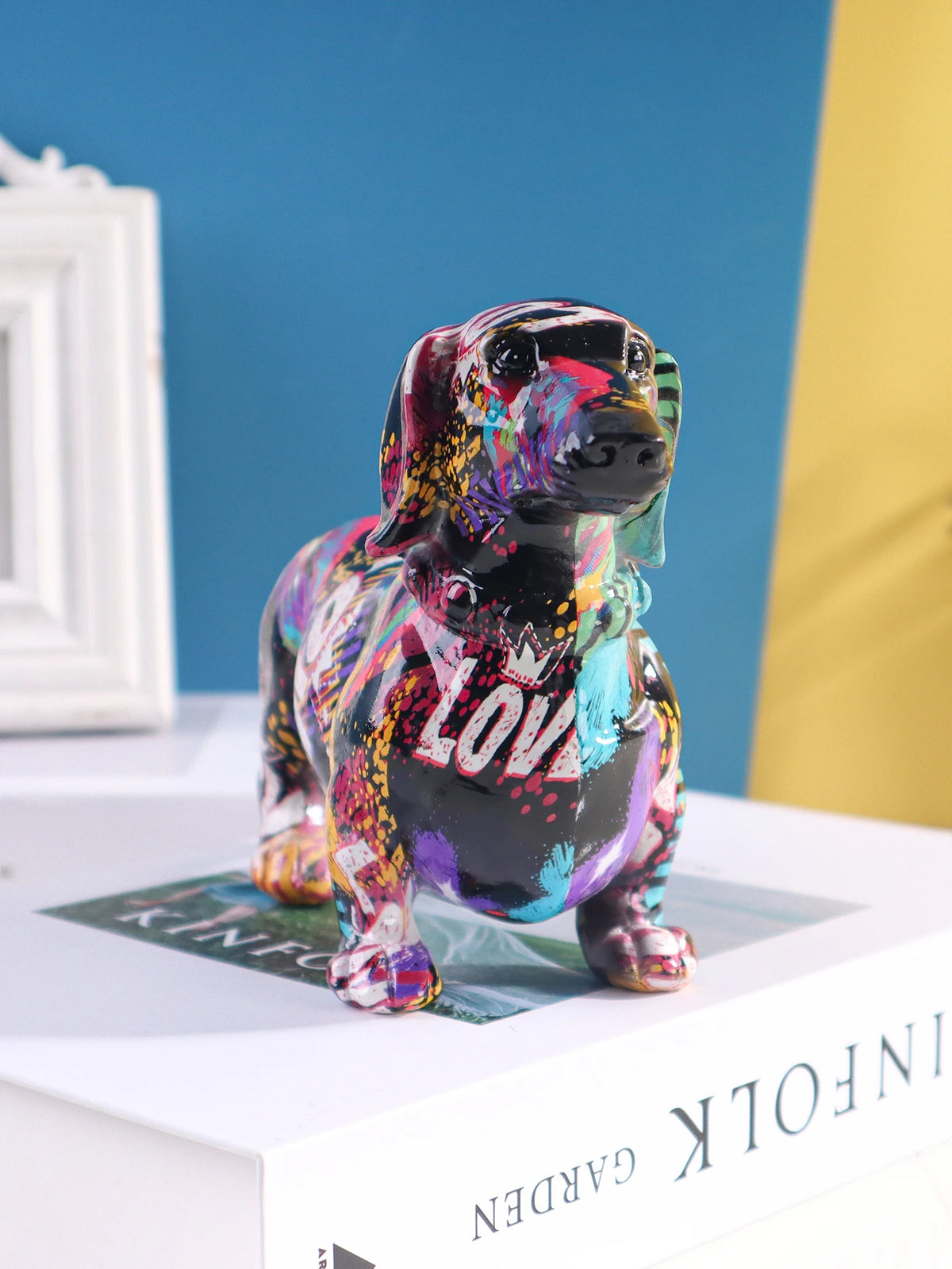 A colorful resin figurine of a dachshund dog in various vibrant colors sitting on a white box.
