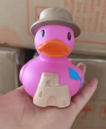 A pink rubber duck bath toy with an orange beak and a gray hat is held in a hand.