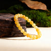 A string of round, yellow citrine crystal beads displayed on a dark wooden surface next to green moss.