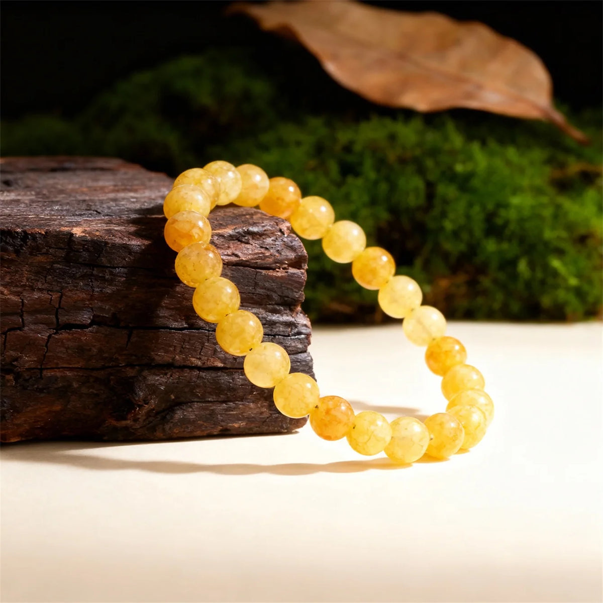 A string of round, yellow citrine crystal beads displayed on a dark wooden surface next to green moss.
