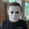 A person wearing a realistic white horror mask with dark features, posing indoors.
