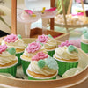 Green cupcake liners filled with white frosting and pink floral decorations