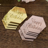 A set of ten rose gold and pink acrylic birthday message toppers stacked on a dark wooden surface.