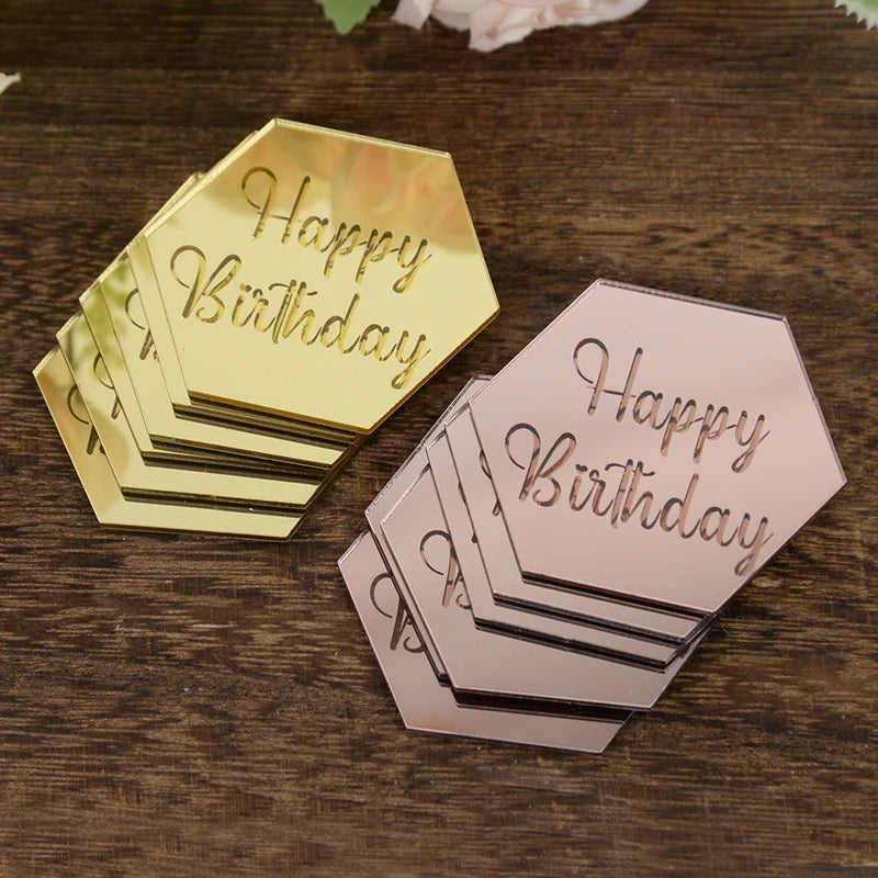 A set of ten rose gold and pink acrylic birthday message toppers stacked on a dark wooden surface.