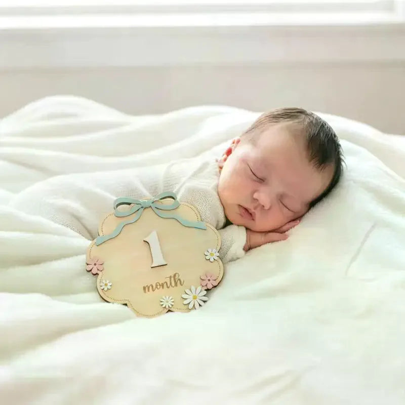 Neugeborenes Baby schläft auf einer weißen Decke neben einem natürlichen Holz-Meilenstein mit der Markierung 1 Monat.