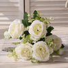A bouquet of white silk peony artificial flowers with green leaves displayed on a white surface.