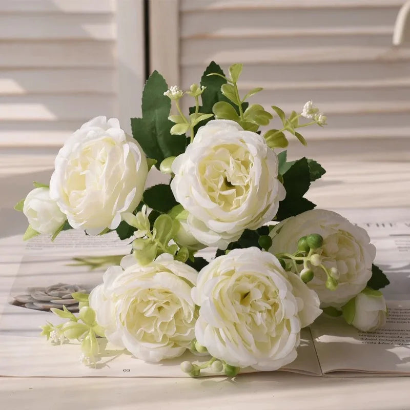 A bouquet of white silk peony artificial flowers with green leaves displayed on a white surface.