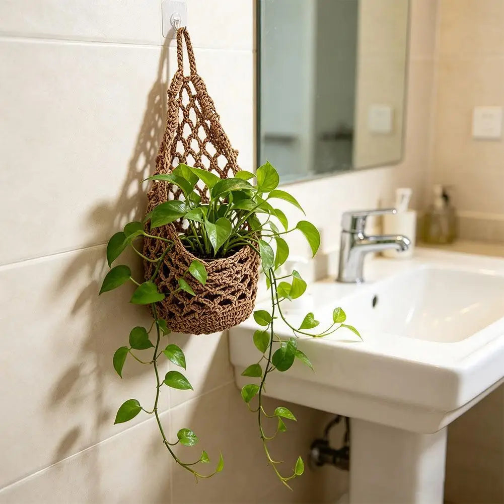A macrame hanging storage basket with green plants is mounted on a white tiled wall above a bathroom sink.