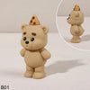 A light tan teddy bear figure with a gold cone topper, shown in a studio setting.