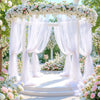 An elegant white tulle floral archway backdrop for events and celebrations surrounded by pink and white flowers.