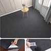 Close-up view of a dark gray self-adhesive runner rug being applied to a wooden floor.