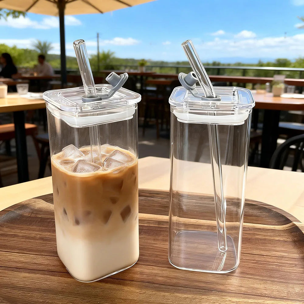 A clear glass coffee mug filled with iced latte sits on a wooden table outdoors.