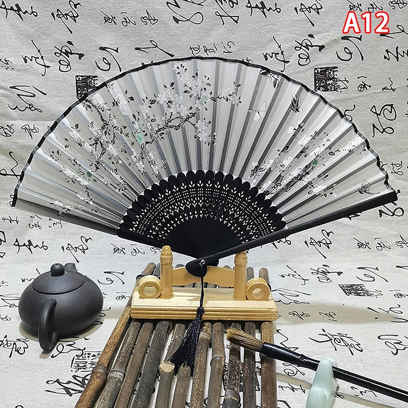 An elegant vintage Chinese folding hand fan with a black frame and silver-edged paper is displayed on a wooden stand.