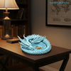 A light blue dragon design decorative tray for jewelry and small items resting on a wooden table.