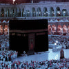 A large crowd of people gathered in front of a dark canvas depicting the Kaaba and Al Masjid An Nabawi.