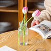 A glass vase holds two pink and white tulips on a wooden table next to an open book.