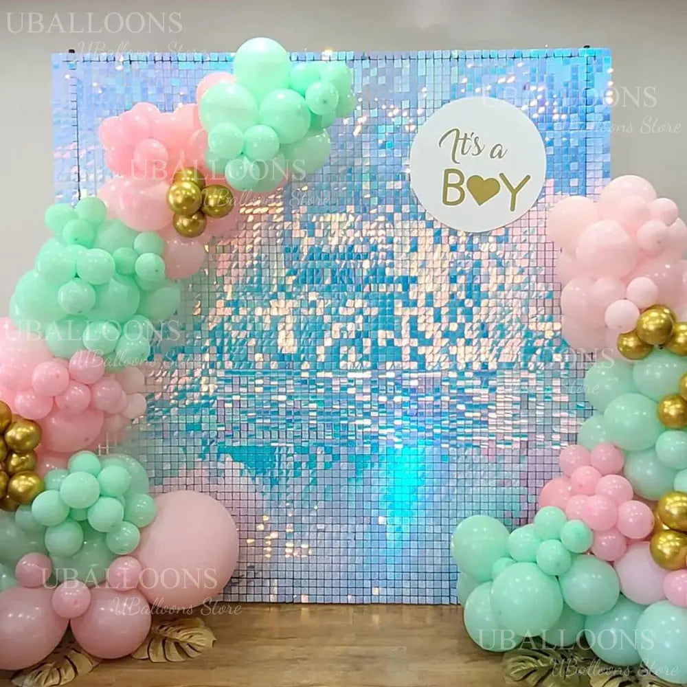 A shimmering pink and green balloon wall backdrop decorated with glitter and gold accents for a party.